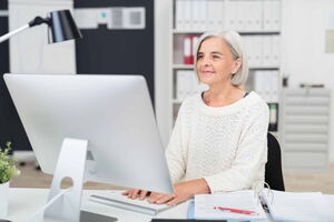 Eine erfahrene Frau sitzt an einem Computerbildschirm und sieht zufrieden aus. Die Arbeit macht ihr Spaß. Ich unterstütze Sie dabei, dass auch Ihnen die Arbeit wieder Spaß macht.
